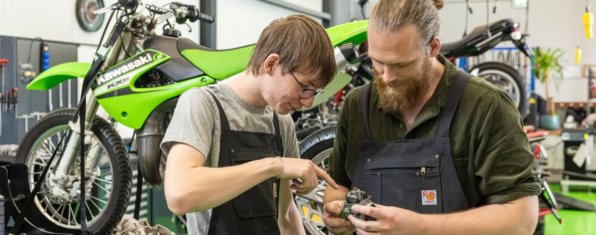 Docent en student staan voor motorfiets te kijken naar onderdeel