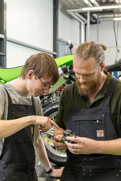 Docent en student staan voor motorfiets te kijken naar onderdeel