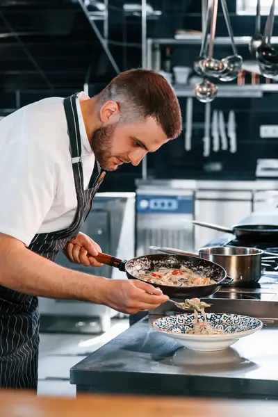Kok schept verse paste op in keuken
