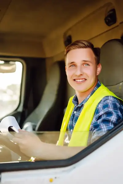 Vrachtwagenchauffeur in geel hesje in cabine vrachtwagen