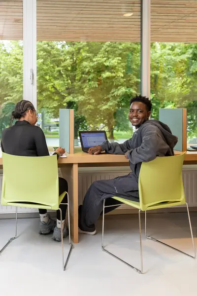 Student achter laptop voor raam op gele stoel