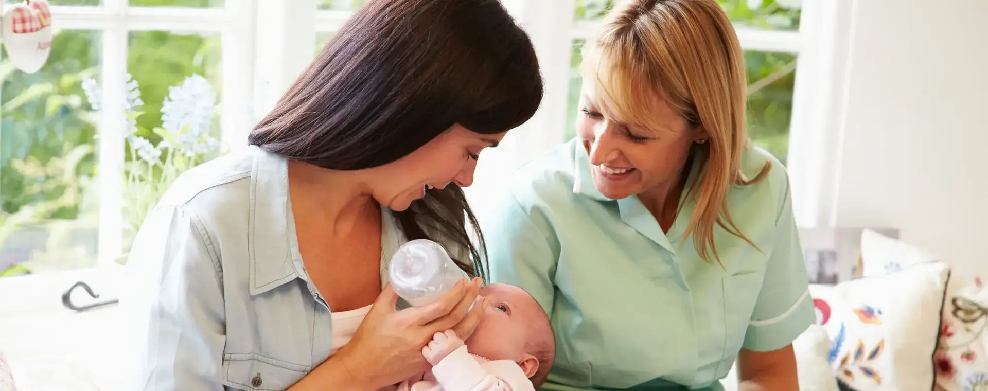 Kraamverzorgende naast vrouw die baby flesvoeding geeft