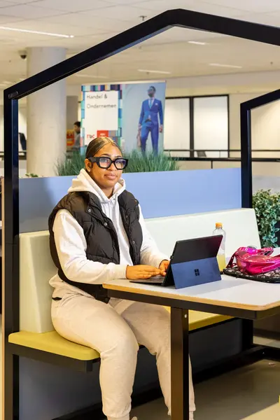 Student zit aan tafel en werkt op een laptop in een open studieruimte.