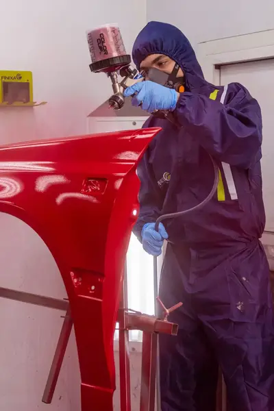 Student in overall verft een auto-onderdeel met spuitbus.