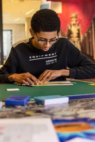 Student aan een tafel vol met knipsels neemt de formaten op van een foto.