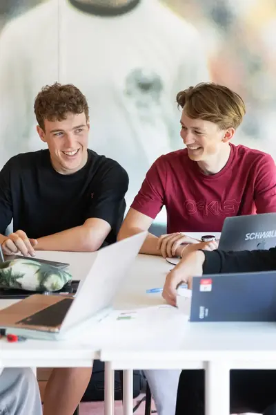 Vier studenten zitten samen een schoolopdracht te maken met open laptops