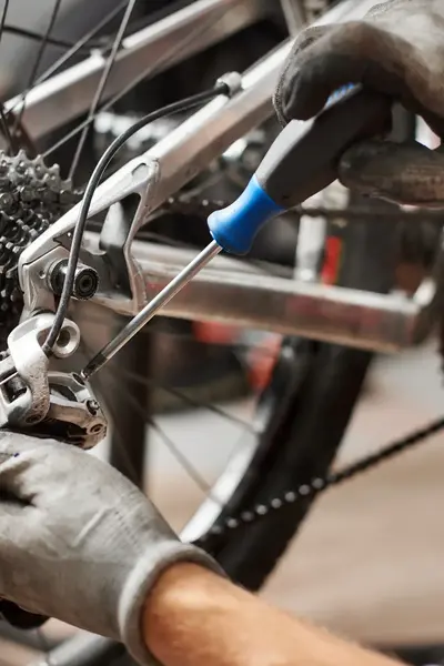Monteur met handschoenen voert onderhoud uit aan de versnelling van een fiets.