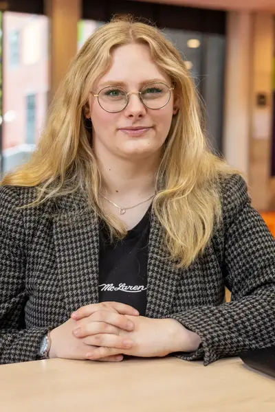 Student met lang blond haar zit aan tafel met een open laptop.