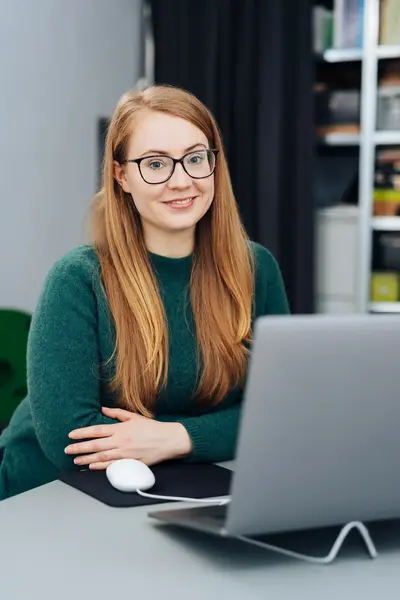 Student met bril zit glimlachend achter een laptop aan een bureau.