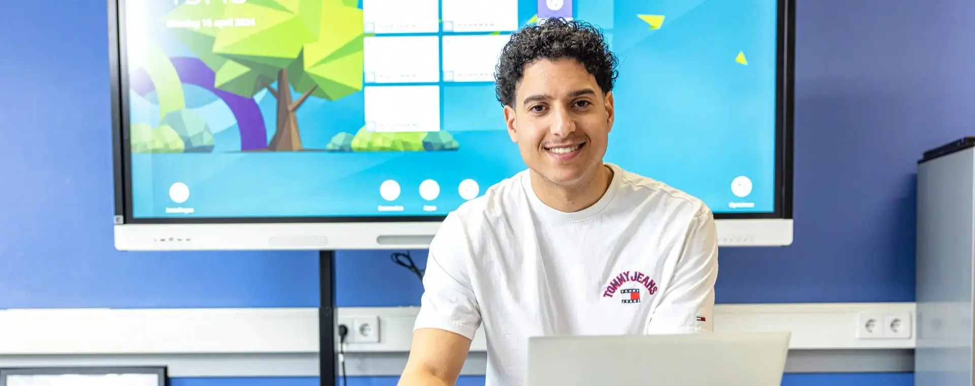 Jongeman achter laptop met groot beeldscherm achter hem
