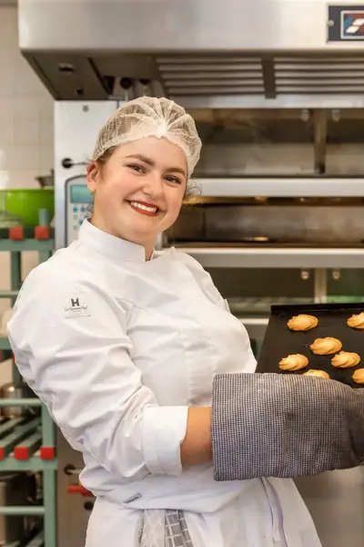 Blije bakker in witte kleding toont bakplaat met versgebakken koekjes.