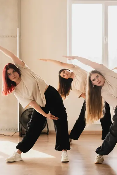 Dansstudenten voeren een groepschoreografie uit in een lichte dansstudio met houten vloer en grote ramen.