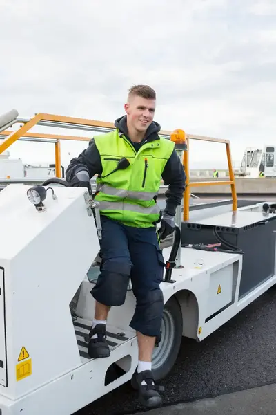 Luchtvrachtmedewerker in geel hesje stapt van bagagevoertuig