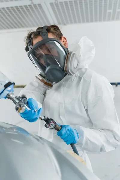 In wit geklede en gemaskerde autospuiter met verfspuit