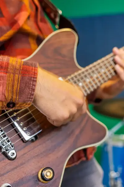 Student speelt gitaar tijdens een muziekles, met op de achtergrond een medestudent op het drumstel.