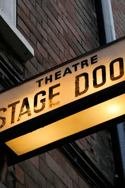 Verlichte ingang van een theater met het bord 'Stage Door'.