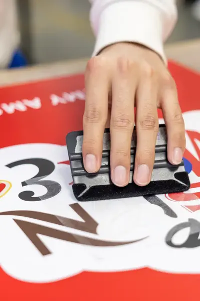 Een hand strijkt met een rakel een grote sticker glad.