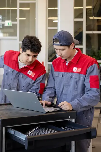 Twee studenten in ROCvA-overall inspecteren motorblok auto via computer