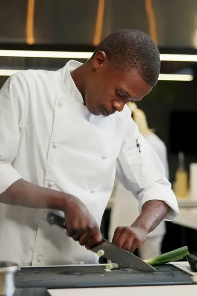 Student in kokstenue snijdt prei in keuken