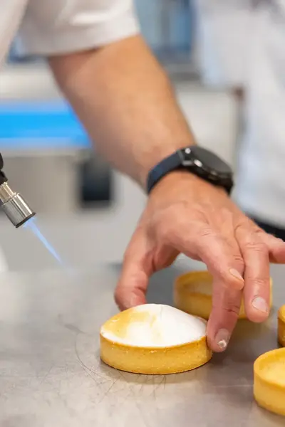Een patissier brandt zorgvuldig de meringue op een tarteletje met een gasbrander.