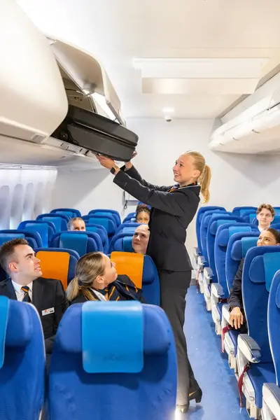 Stewardess bergt een koffertje op in de handbagage ruimte.
