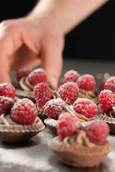 Chocoladetartelettes met frambozen worden bestrooid met poedersuiker.