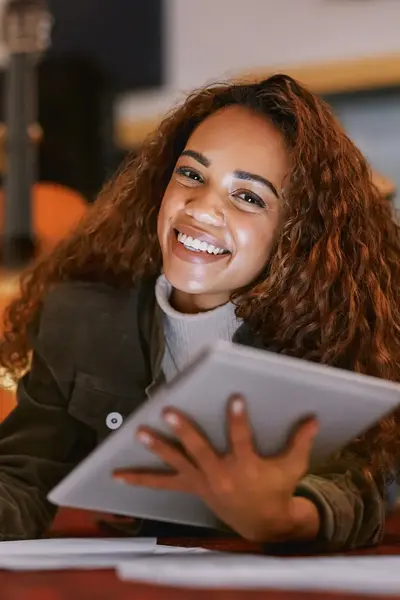 Student zit in een muzieklokaal met een pen en tablet in de hand en glimlacht naar de camera.