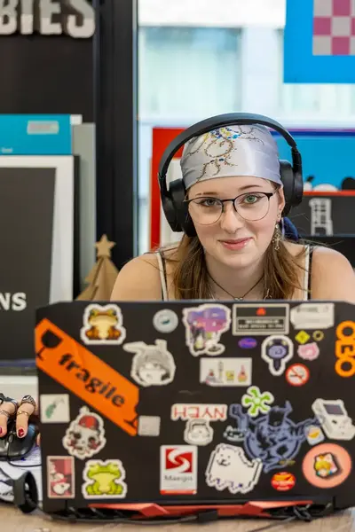 Studente met koptelefoon op zit achter een laptop vol met stickers.