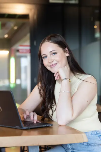 Studente achter laptop kijkt glimlachend in de camera.