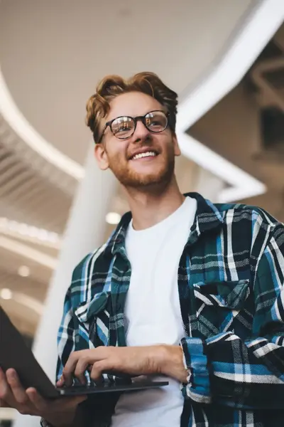 Staande student vanonder gefotografeerd met een laptop in de hand.