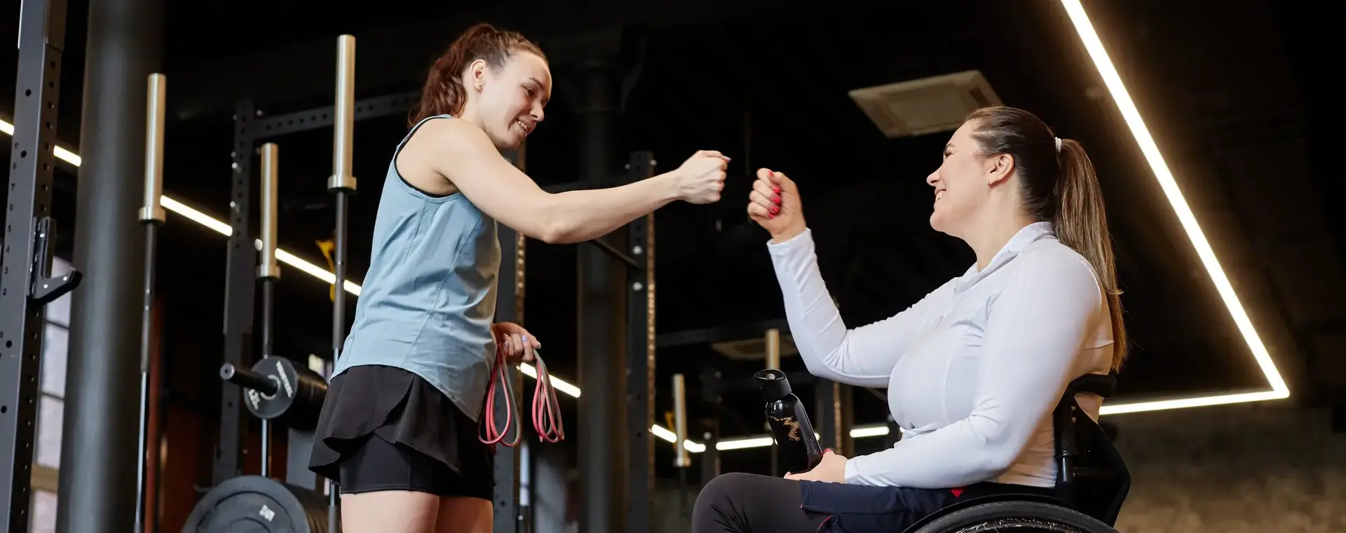 Trainer met vrouw in rolstoel in een fitnessruimte geven elkaar een box