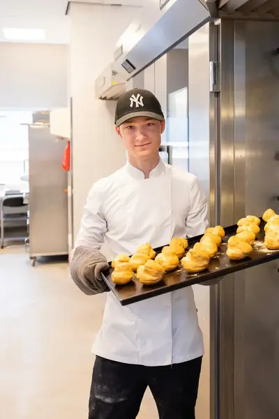 Bakker haalt een bakplaat met versgebakken soezen uit de oven.