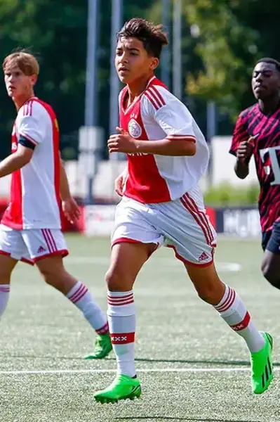 Jeugdspelers van Ajax voetballen op het veld tijdens een wedstrijd.