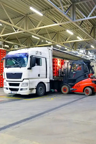 Witte vrachtwagen wordt gevuld door heftruckbestuurder in magazijn.