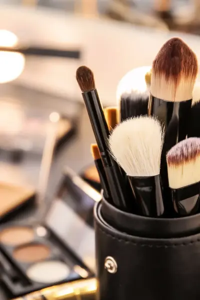 Close-up van make-upkwasten in een zwarte houder, omringd door foundations, poeders en paletten.