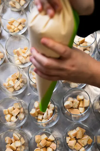 Kok spuit dessertcrème in glazen met stukjes cake.