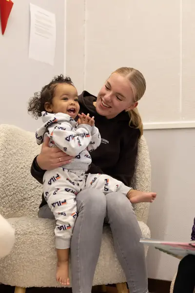 Studente op kinderopvang met kind op schoot en kind met boek ernaast
