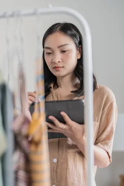 Studente met tablet inventariseert kledingvoorraad