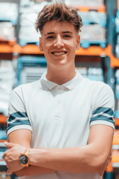 Jongeman staat met zijn armen over elkaar voor stellages met voorraden in een magazijn.