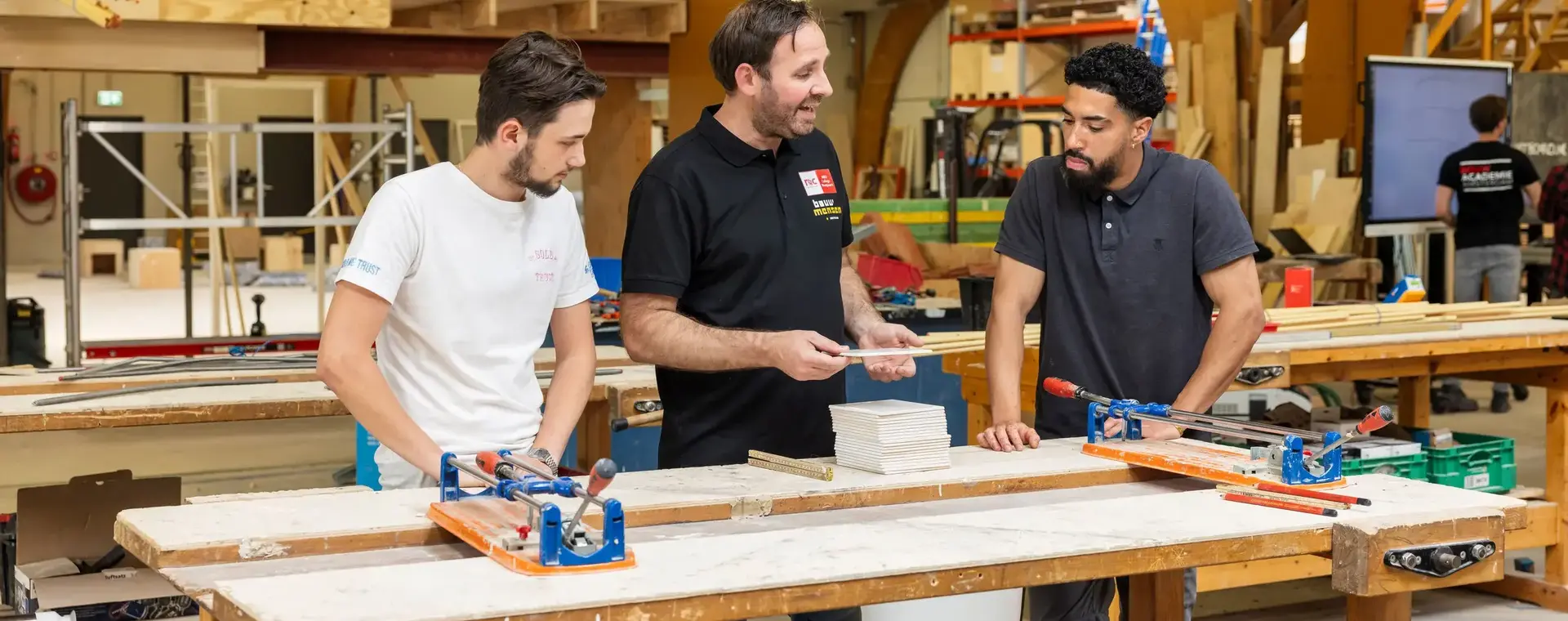 Studenten leren werken met hout onder begeleiding van een docent op de werkplaats.
