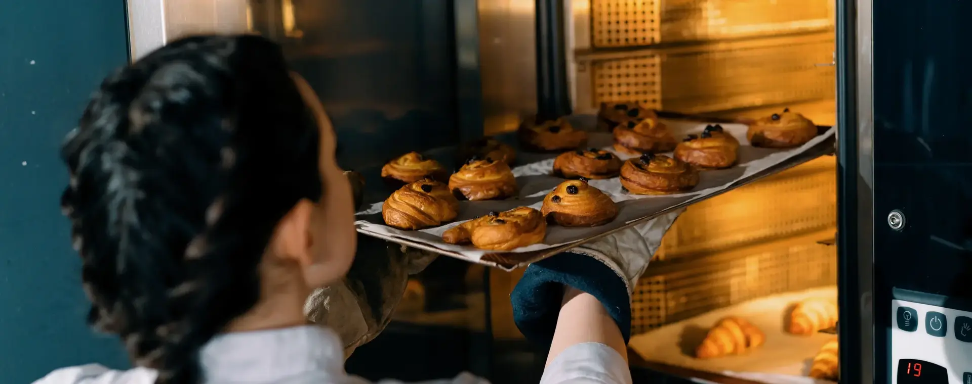 Bakker plaatst een tray met verse broodjes in de oven
