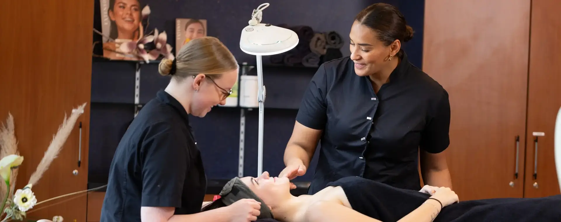 Student oefent een behandeling onder begeleiding van een docent. Ze werken geconcentreerd samen in een salonruimte met professionele apparatuur.