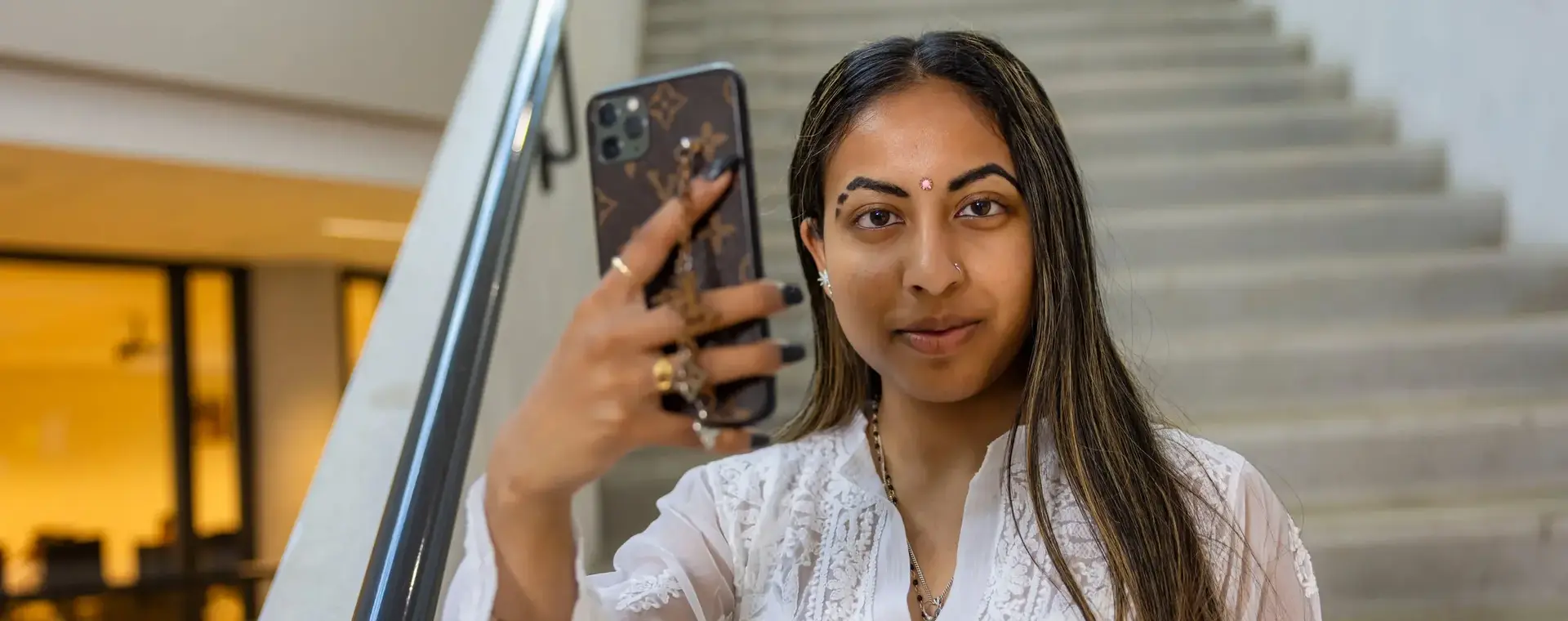Student zit op een trap van de school en maakt een selfie of vlog met haar eigen mobiele telefoon.