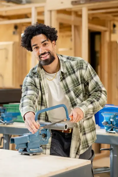 Jonge man in een timmer werkplaats staat bij een werktafel en is een kunststof buis aan het afzagen met een handzaag.