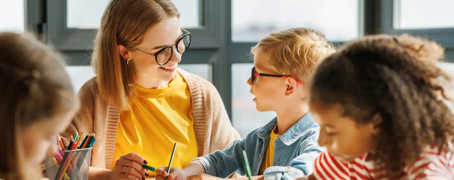 Juffrouw met zwarte bril aan tafel met basisschoolkinderen