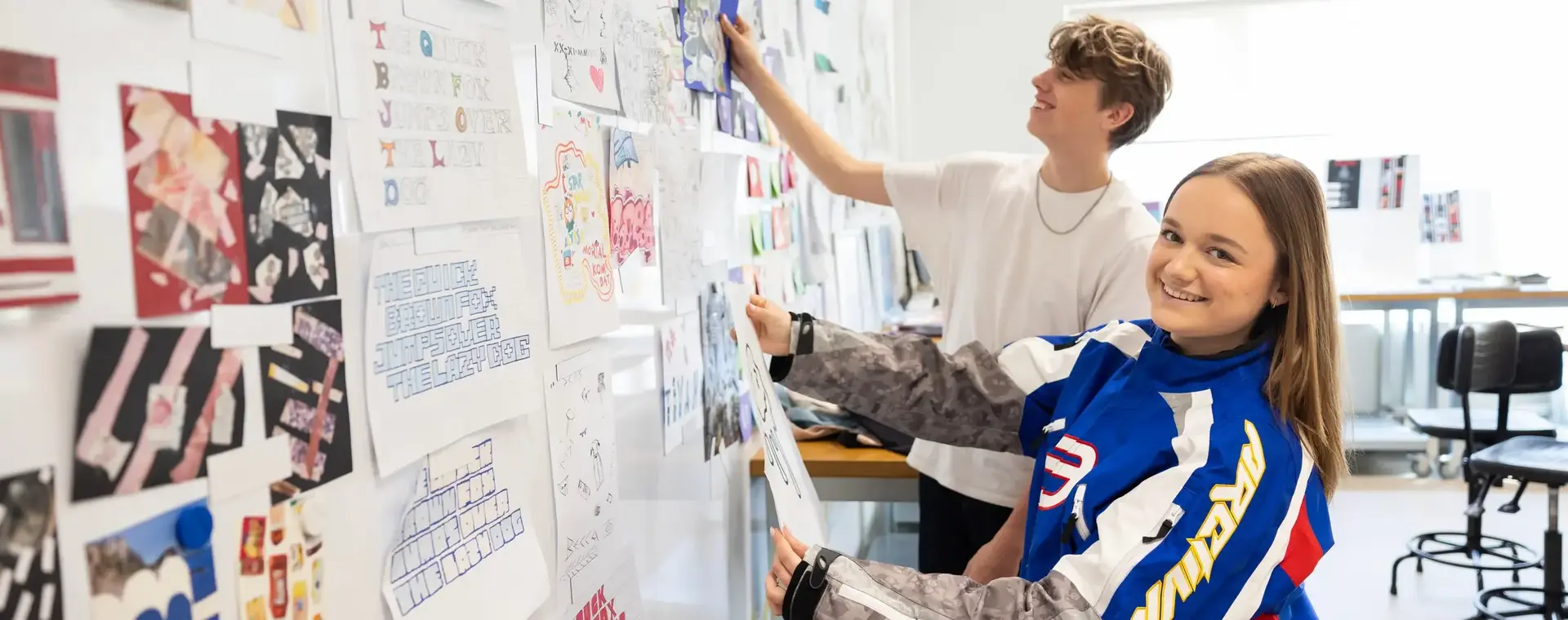 Studenten Media en Vormgeving hangen hun creaties aan de muur.