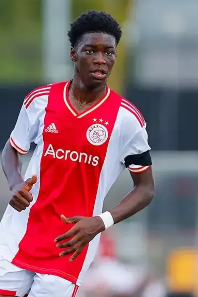 Ajax-jeugdspeler in rood-wit tenue rent over het veld tijdens een wedstrijd.