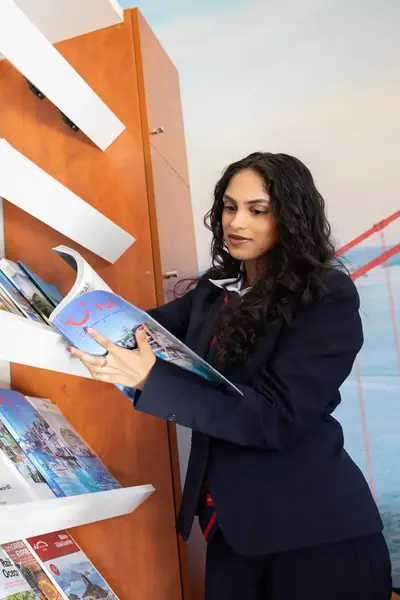 Studente Toerisme en Recreatie bekijkt vakantiefolders bij rek vakantiefolders.
