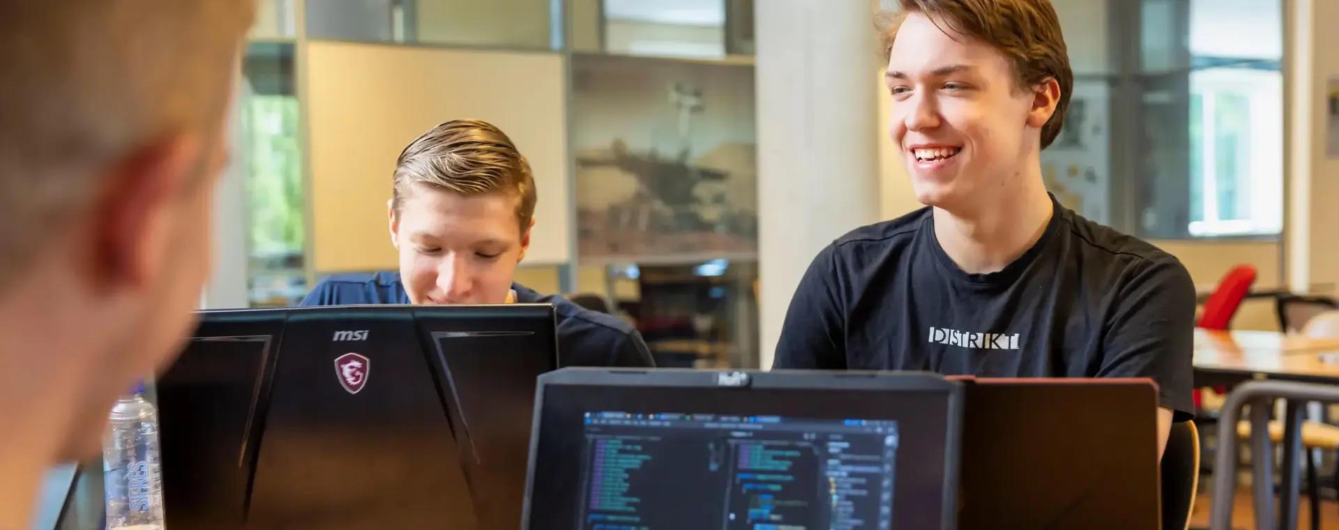 Studenten werken samen aan programmeeropdrachten met laptops in een klaslokaal