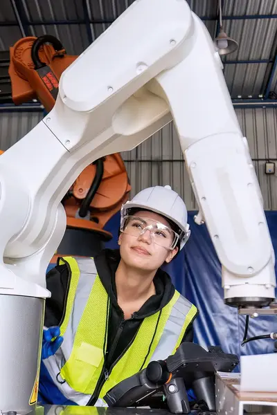 Student met helm en veiligheidsbril bestudeert witte robotarm